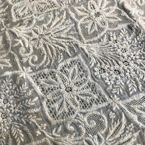 以下が含まれることがあります： 白い綿の生地に、複雑な白い花の刺繍が施されています。