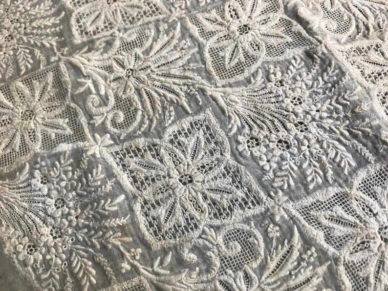 以下が含まれることがあります： 白い綿の生地に、複雑な白い花の刺繍が施されています。