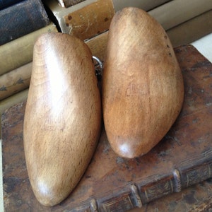 May include: Two wooden shoe trees, one on top of the other, with a light brown finish. The shoe trees are on top of a stack of old books.