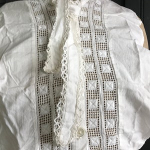 以下が含まれることがあります： 繊細なレースのトリムと刺繍のディテールが施された白いコットンカラー。カラーはボタン留めとフリルエッジになっています。