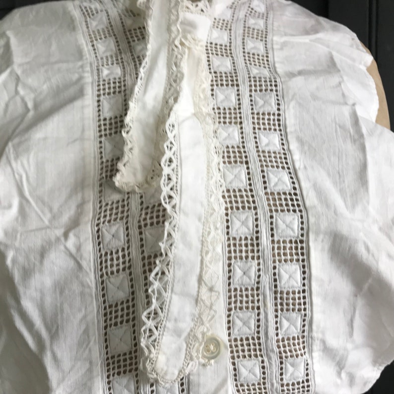 以下が含まれることがあります： 繊細なレースのトリムと刺繍のディテールが施された白いコットンカラー。カラーはボタン留めとフリルエッジになっています。