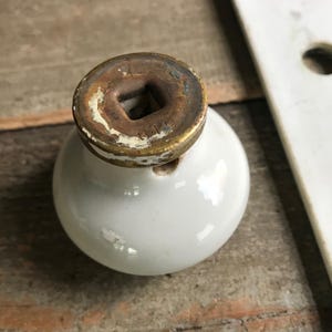 May include: White ceramic door knob with a brass base. The base has a square hole and the inscription "B119" on it.
