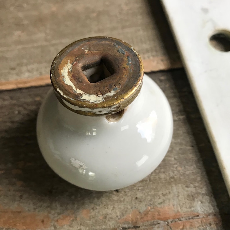 May include: White ceramic door knob with a brass base. The base has a square hole and the inscription "B119" on it.