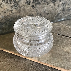 May include: A clear glass jar with a lid, both with a cut-glass diamond pattern. The jar is sitting on a wooden surface.