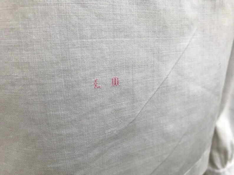 May include: White linen fabric with a small pink embroidered mark that reads "L.M."