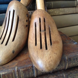 May include: Two vintage wooden shoe forms with slotted tops. The shoe trees are light brown and sit on a stack of antique books. The shoe forms have a classic design, perfect for preserving the shape of shoes.