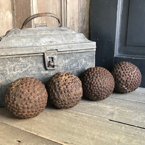 Può includere: Quattro palle di legno marroni con borchie metalliche, disposte in fila su una superficie di legno. Una scatola di metallo vintage con maniglia è sullo sfondo.