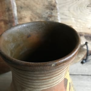 May include: A brown clay vase with a wide opening and a striped pattern in shades of brown and white.