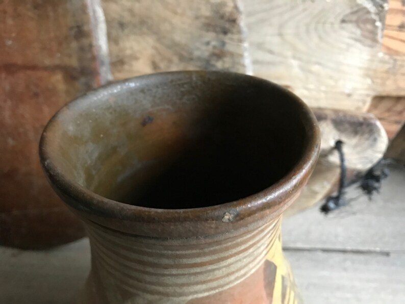 May include: A brown clay vase with a wide opening and a striped pattern in shades of brown and white.