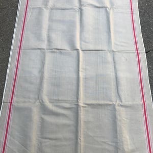 以下が含まれることがあります： 赤色のストライプが縁取りされた、大きなオフホワイトのリネン製のテーブルクロスです。