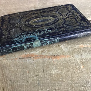 May include: A vintage, blue leather-bound book with gold and teal embellishments. The book has a worn, antique look and features intricate floral designs.