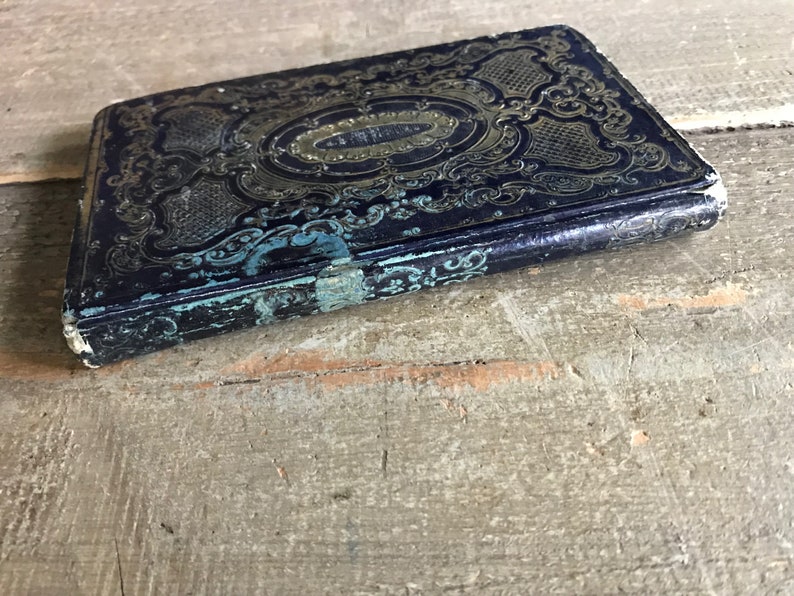 May include: A vintage, blue leather-bound book with gold and teal embellishments. The book has a worn, antique look and features intricate floral designs.