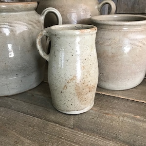 May include: Three ceramic crocks in various sizes, all in a light grey colour with brown speckles. The crocks have a rustic, handmade look.