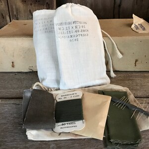 May include: A vintage sewing kit with two white cotton drawstring bags, a spool of green thread labeled "Barbour's No. 35 - 2 Cord 50 Yards Rotproofed", two pieces of green fabric, a small brown envelope, and a needle holder with needles.