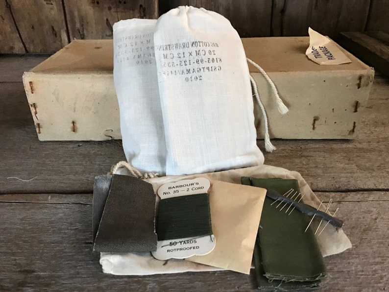 May include: A vintage sewing kit with two white cotton drawstring bags, a spool of green thread labeled "Barbour's No. 35 - 2 Cord 50 Yards Rotproofed", two pieces of green fabric, a small brown envelope, and a needle holder with needles.