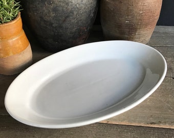 May include: A large, white oval serving platter made of ceramic. The platter is sitting on a wooden surface.