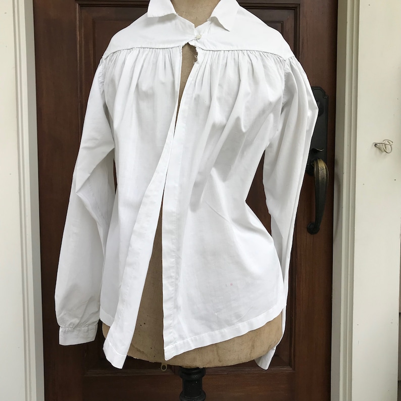 May include: A white long-sleeved shirt with a gathered neckline and a split front opening. The shirt is made of a lightweight fabric and has a classic, simple design.