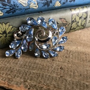 May include: A silver brooch with a swirling design and light blue teardrop-shaped rhinestones.