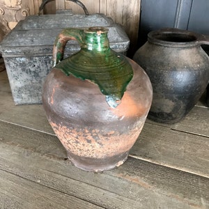 以下が含まれることがあります： 緑色の釉薬がかかった茶色の陶器の壺。壺は木の表面の上に置かれている。