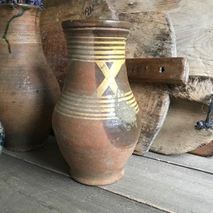May include: Three brown ceramic jugs with yellow and brown painted designs. The jugs are sitting on a wooden surface.