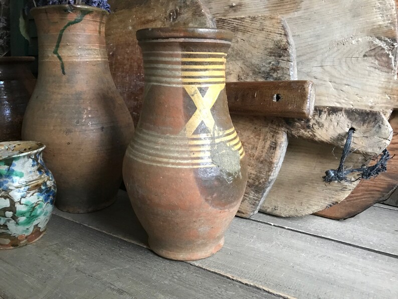May include: Three brown ceramic jugs with yellow and brown painted designs. The jugs are sitting on a wooden surface.