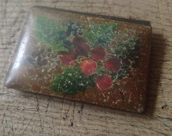May include: A small, rectangular, brown box with a holly and berry design. The box is made of a textured material and has a worn, vintage look.