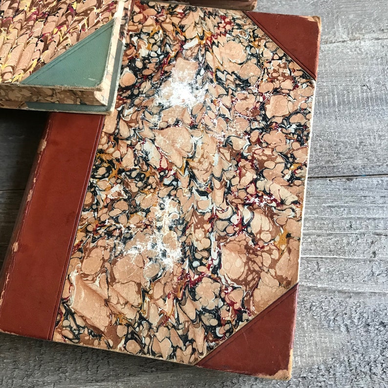 May include: A vintage book with a marbled cover in shades of brown, red, black, and white. The book has a red leather spine and corners.