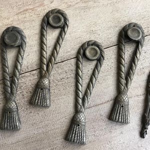May include: Five antique-style metal drawer pulls with a rope design and a tassel at the bottom. The pulls are in a silver finish.