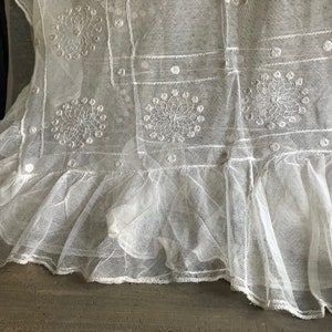May include: White lace fabric with a ruffled hem and embroidered floral designs.