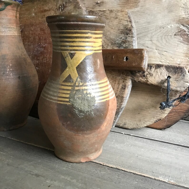 May include: A brown ceramic pitcher with a yellow and brown geometric design. The pitcher has a wide base and a narrow neck.
