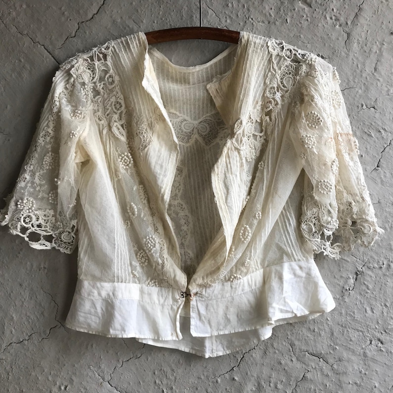 May include: A white lace top with a ruffled hem and short sleeves. The top is made of delicate lace and has a button closure in the front.