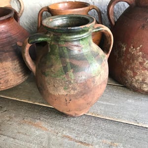 Puede incluir: Una colección de cuatro jarras de cerámica de terracota con esmalte verde y marrón. Las jarras tienen dos asas y son de varios tamaños.