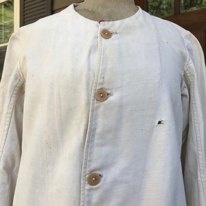 K&ouml;nnte beinhalten: Cremefarbene Jacke mit rundem Kragen und drei Holzkn&ouml;pfen. Die lang&auml;rmlige Jacke weist Gebrauchsspuren auf. Der Stoff ist ein robustes, gewebtes Material. Vintage-Stil Jacke.