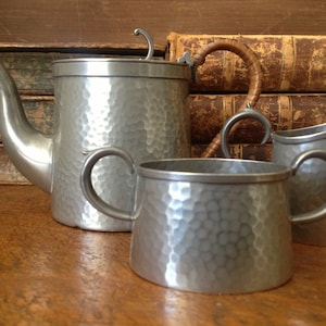 May include: A silver tea set with a hammered finish. The set includes a teapot, creamer, and sugar bowl.
