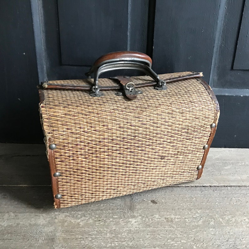 May include: A vintage woven wicker suitcase with a brown leather handle and metal accents. The suitcase has a rectangular shape and is made of natural materials.