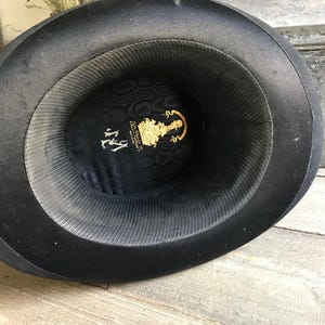 May include: Black top hat with a black satin lining and a gold label with the text "The Gentleman's Hat Company, NY".