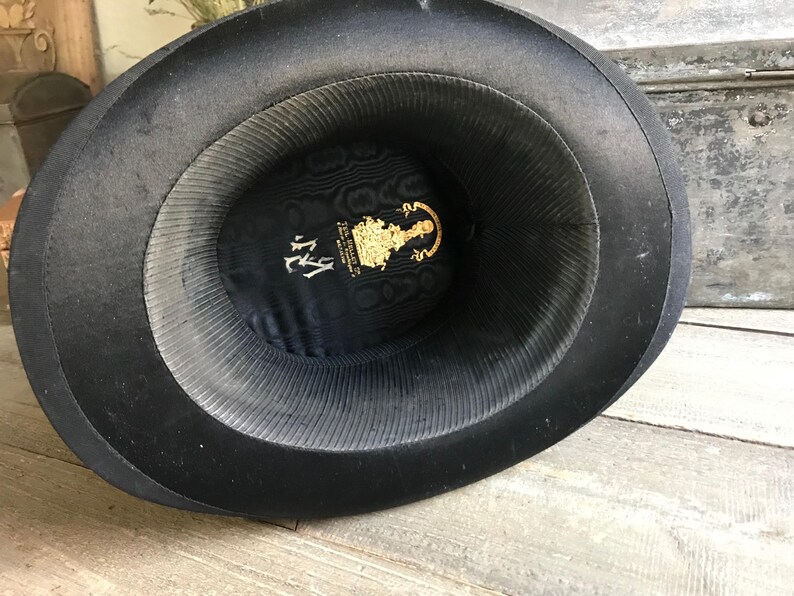 May include: Black top hat with a black satin lining and a gold label with the text "The Gentleman's Hat Company, NY".
