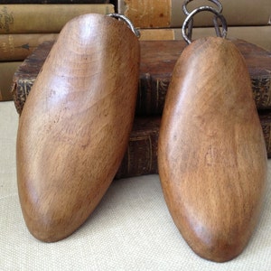 May include: Two wooden shoe trees with metal hooks. The shoe trees are brown and have a smooth finish.