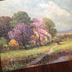 May include: A vintage jigsaw puzzle depicting a quaint cottage nestled amongst blooming trees and a winding path leading to a bridge over a stream. The scene is painted in soft, pastel colors, creating a peaceful and idyllic atmosphere.