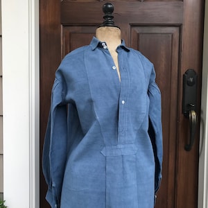 May include: A blue linen shirt with a white collar and button-up front. The shirt has a pleated detail down the front and long sleeves.