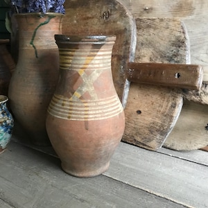 May include: A collection of four brown clay pottery jugs with various designs. The jugs are arranged on a wooden surface. The jugs are all different sizes and shapes.
