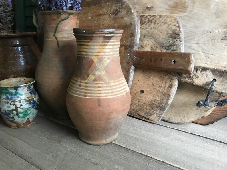 May include: A collection of four brown clay pottery jugs with various designs. The jugs are arranged on a wooden surface. The jugs are all different sizes and shapes.