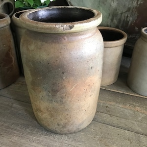 May include: A collection of four vintage stoneware crocks in various shades of brown and grey. The crocks are all different sizes and have a rustic, antique look.