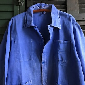 May include: A blue work jacket with a button-up front and multiple pockets. The jacket is made of a sturdy, durable fabric and has a classic workwear style.
