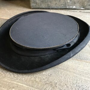 May include: A black top hat with a wide brim and a tall, cylindrical crown. The hat is made of felt and has a smooth, polished finish.