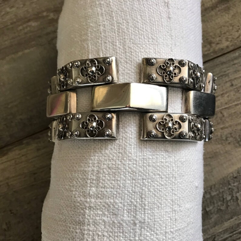 May include: A silver bracelet with a decorative design of interlocking links and floral patterns.