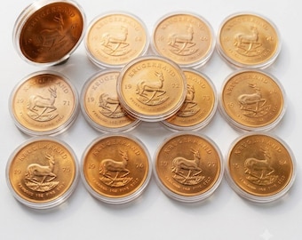 Könnte beinhalten: Eine Sammlung von zwölf goldenen Krugerrand-Münzen, die jeweils in einer durchsichtigen Kunststoffkapsel eingeschlossen sind. Die Münzen zeigen das ikonische Springbock-Motiv, den Schriftzug KRUGERRAND sowie verschiedene Prägejahre von 1967 bis 1984.