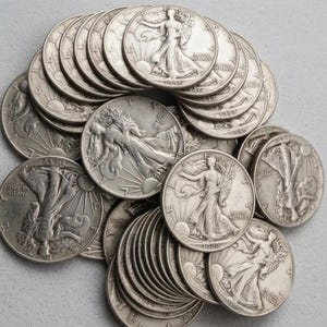 May include: A collection of silver Walking Liberty half-dollar coins stacked and overlapping. Each coin features the figure of Lady Liberty walking toward the left, carrying branches, with the text IN GOD WE TRUST and various dates visible.