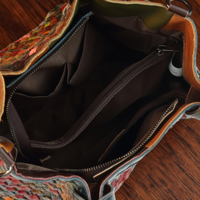 Puede incluir: Un bolso con exterior trenzado que presenta un patr&oacute;n multicolor de tiras de cuero rojas, naranjas, verdes y azules. El interior est&aacute; forrado con tela marr&oacute;n oscuro e incluye un compartimento central con cremallera y bolsillos laterales.