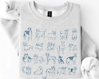 Könnte beinhalten: Ein hellgraues Sweatshirt mit Rundhalsausschnitt und einem sich wiederholenden Muster aus verschiedenen Hunderassen, die mit dunkelblauer Tinte illustriert sind. Das langärmelige Kleidungsstück hat gerippte Bündchen und einen Saum.
